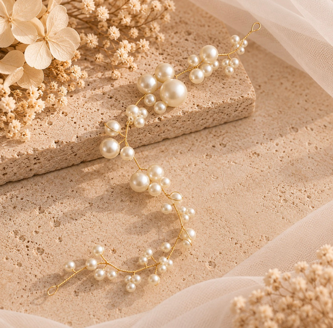A delicate gold vine-style hair claw clip adorned with faux pearls, styled on a textured beige stone block with dried flowers and sheer white fabric.